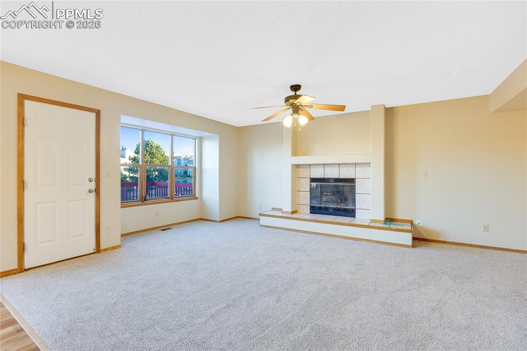 Image 9 of 32: Unfurnished living room with a fireplace, a ceiling fan, and light colored 