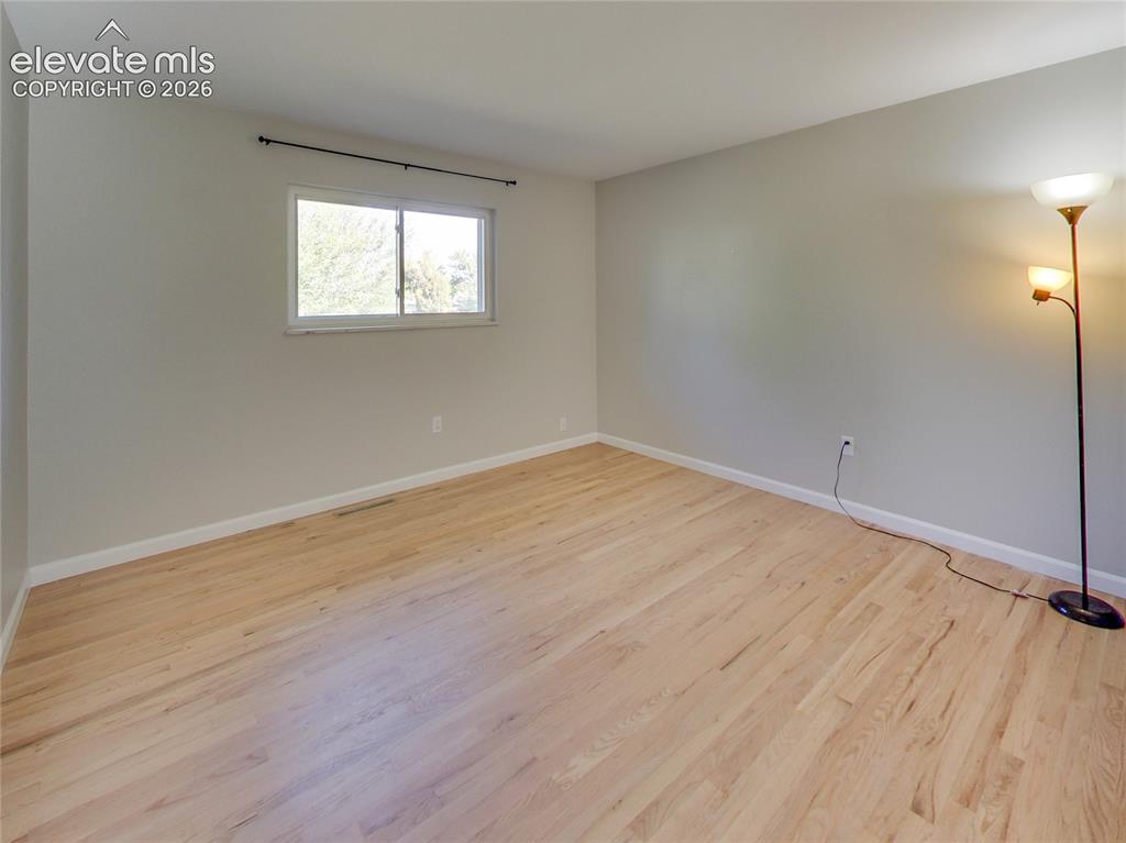 Image 16 of 32: Light wood-finish flooring, white trim, and a window with a black curtain r