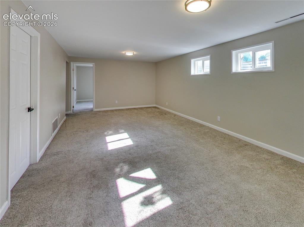 Image 22 of 32: Expansive room featuring neutral-toned walls, gray carpet flooring, two flu