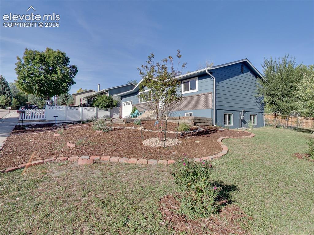Image 27 of 32: Split-level exterior with blue siding and a brick accent, featuring a white