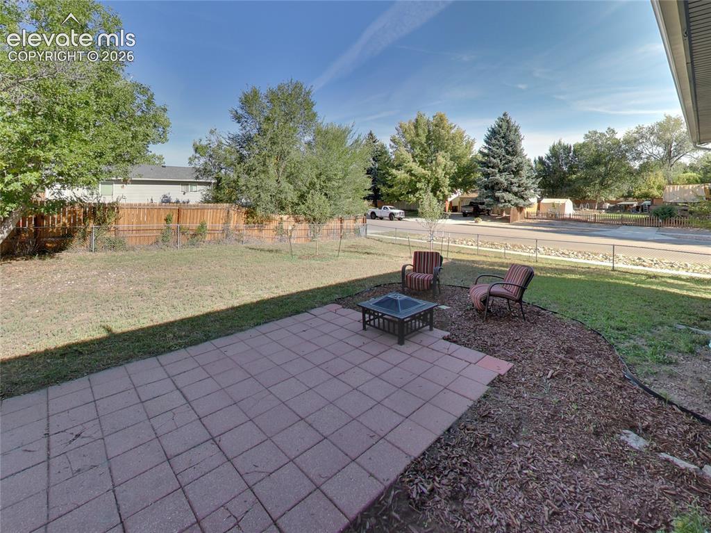Image 29 of 32: Paved patio area, expansive lawn, perimeter fencing, mature trees, and a la