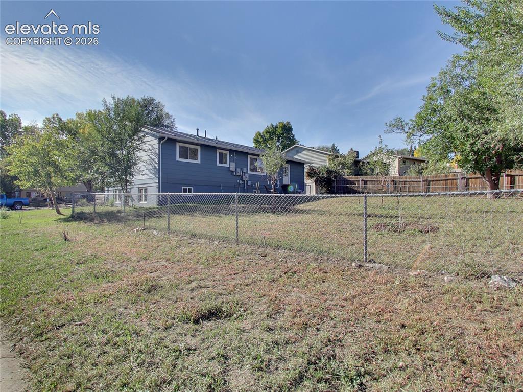 Image 31 of 32: Expansive yard space featuring a chain-link fence, mature trees, and a resi