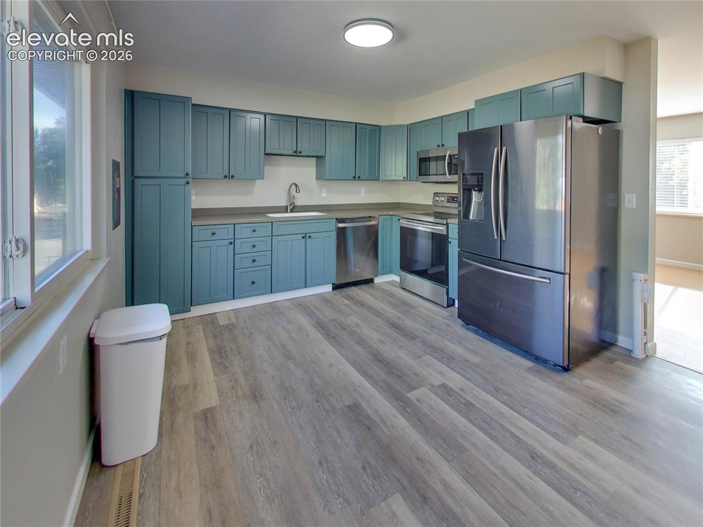 Image 5 of 32: Kitchen featuring wood-finish flooring, teal cabinetry, stainless steel app