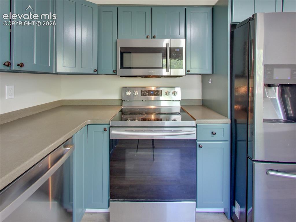 Image 6 of 32: Kitchen featuring blue cabinetry, stainless steel appliances, and solid sur