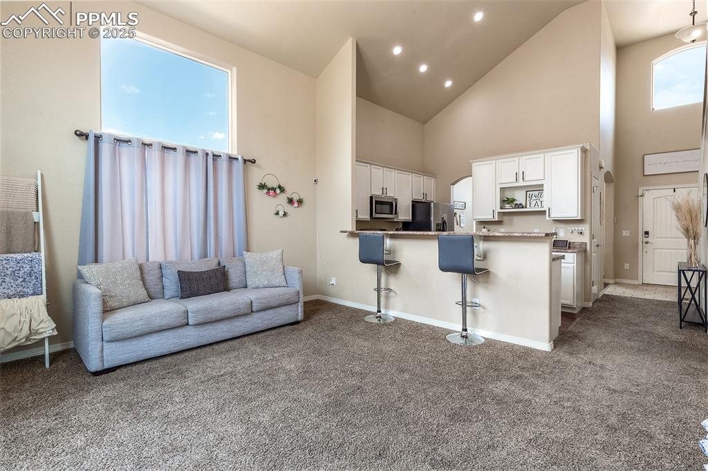 Image 11 of 33: Kitchen featuring dark carpet, white cabinets, high vaulted ceiling, a kitc