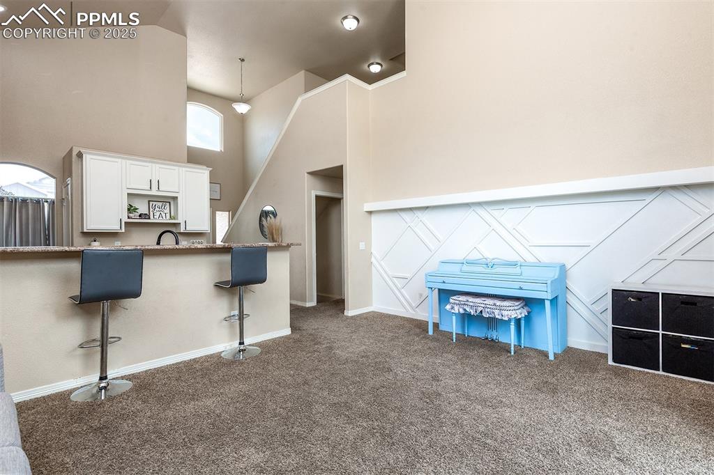 Image 12 of 33: Kitchen with dark colored carpet, high vaulted ceiling, white cabinets, a b