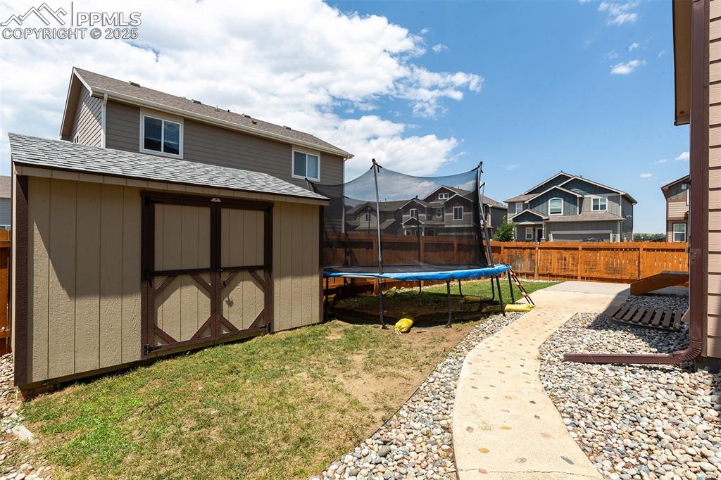 Image 32 of 33: Fenced backyard with a trampoline, a storage unit, a residential view, and