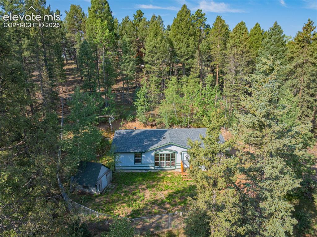Image 22 of 27: Single-story residence set on a sloped lot surrounded by mature evergreen t