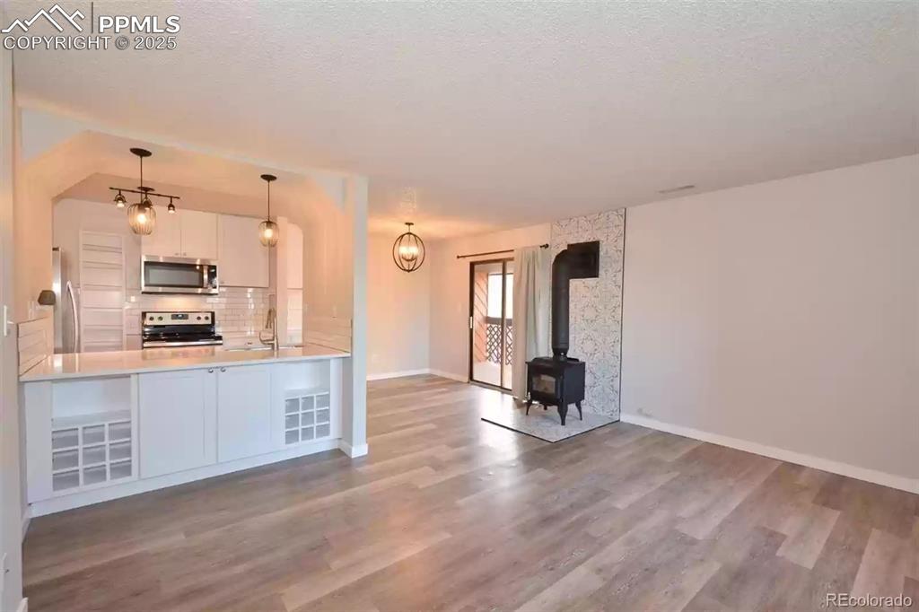 Image 4 of 28: Kitchen with a wood stove, white cabinetry, hanging light fixtures, applian