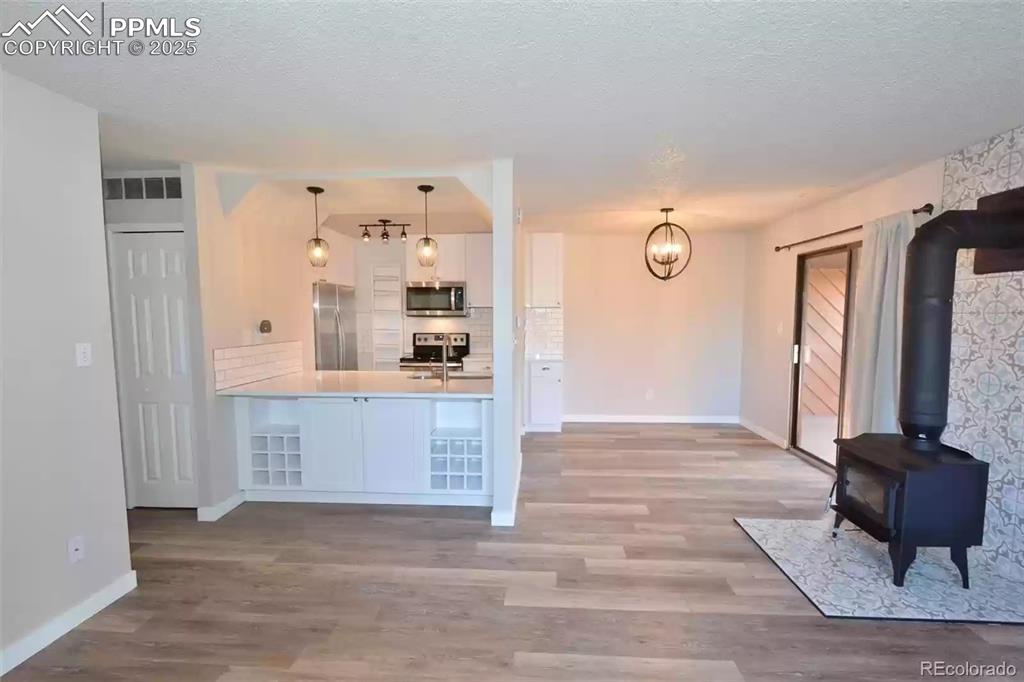 Image 5 of 28: Kitchen with a wood stove, a peninsula, white cabinets, decorative light fi