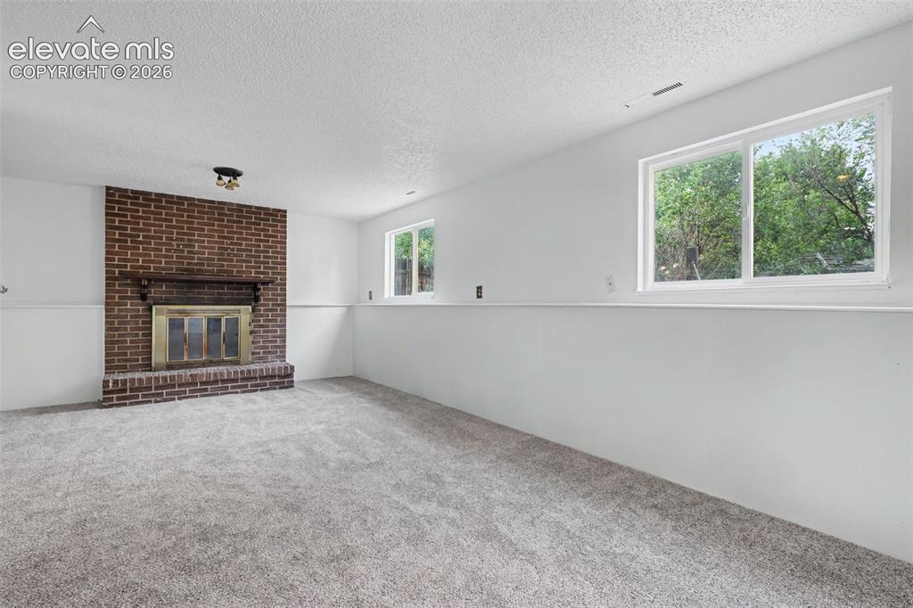 Image 11 of 32: Spacious lower level family room with wood burning brick fireplace.