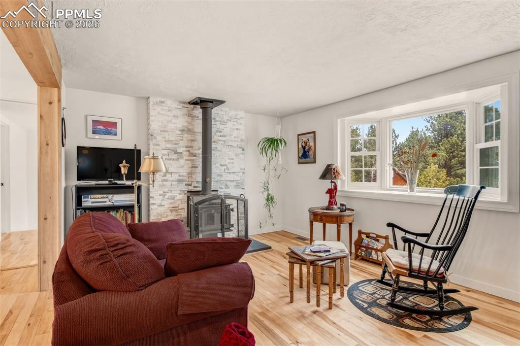 Image 4 of 31: Open concept living room with wood flooring, bay windows, and a wood burnin