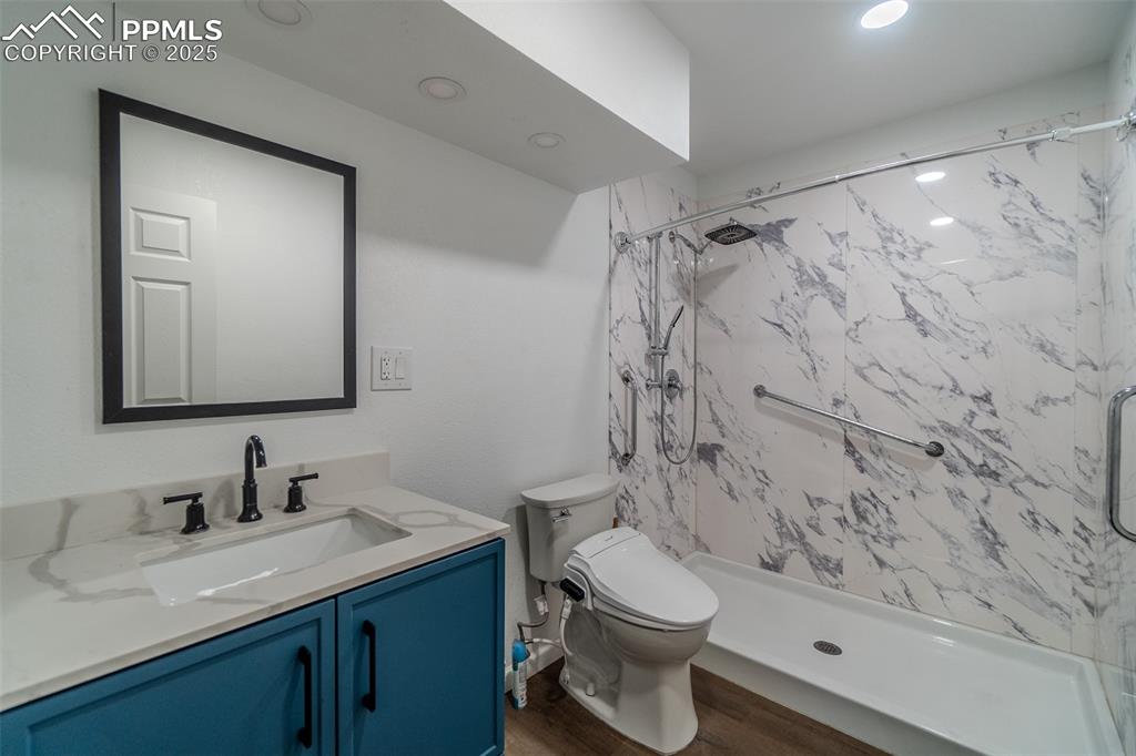 Image 24 of 36: Bathroom with a marble finish shower, vanity, dark wood-style floors, and r
