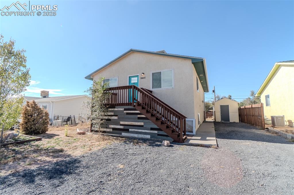 Image 29 of 36: Back of property featuring stucco siding, stairs, and gravel driveway
