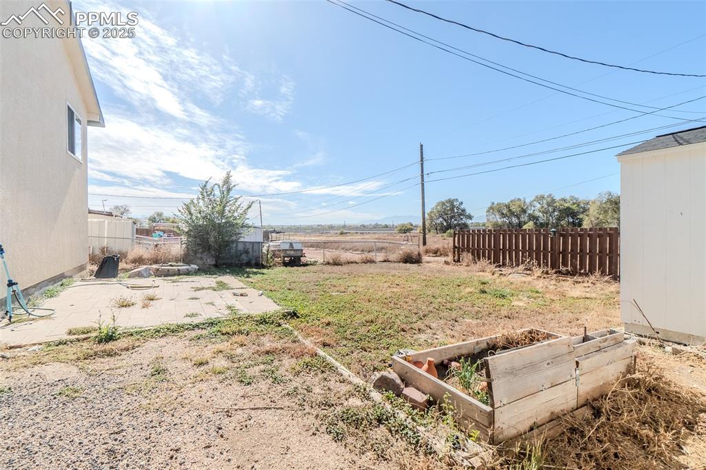 Image 30 of 36: Fenced backyard with a patio area and a vegetable garden