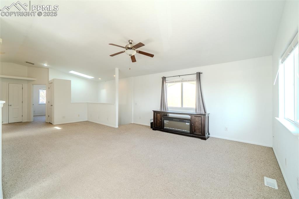 Image 6 of 36: Unfurnished room with a skylight, light carpet, ceiling fan, and vaulted ce