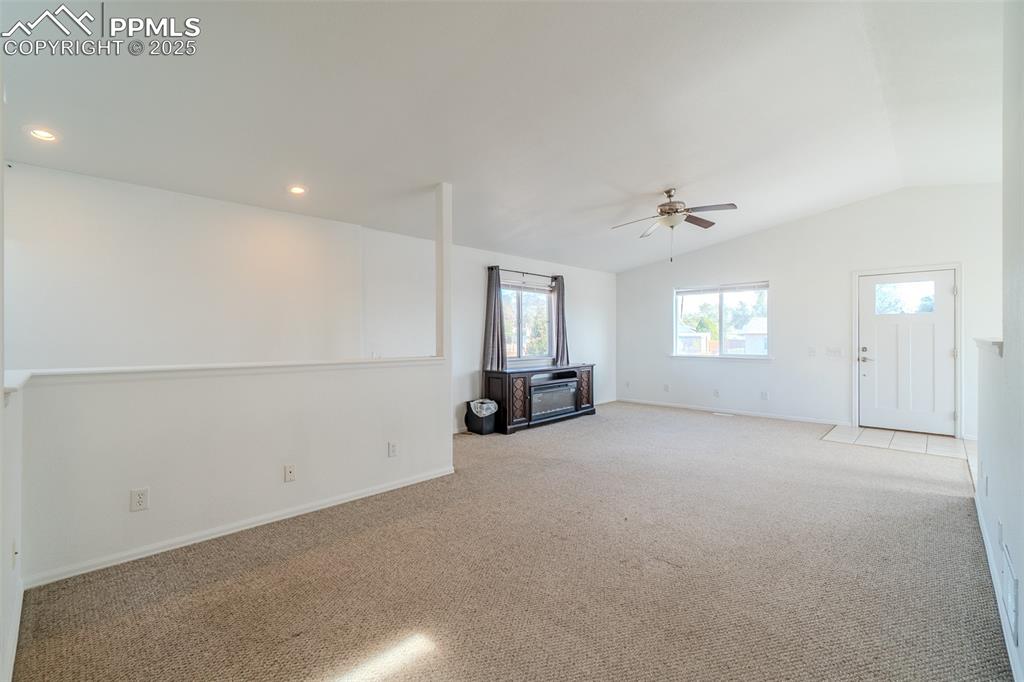 Image 9 of 36: Unfurnished living room with carpet floors, vaulted ceiling, ceiling fan, a