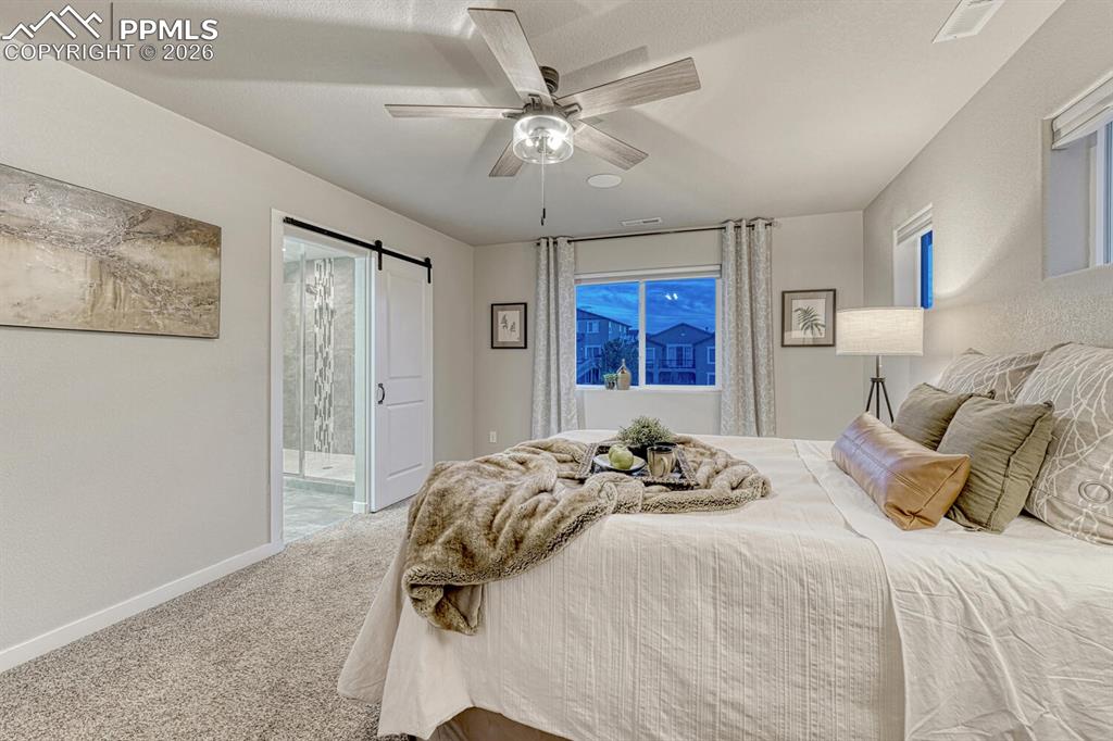 Image 31 of 50: Bedroom with a barn door, carpet flooring, ensuite bathroom, and ceiling fa