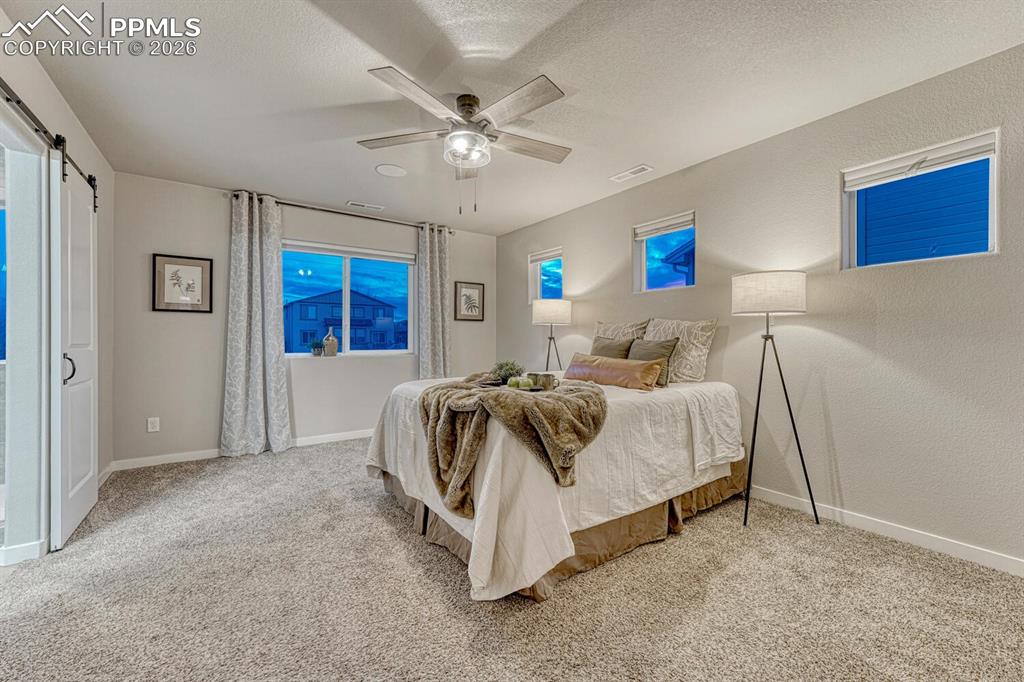 Image 32 of 50: Bedroom featuring a ceiling fan, light colored carpet, a textured wall, a t