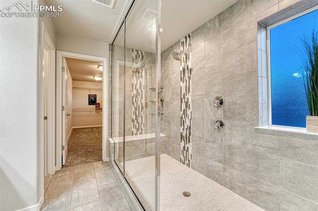 Image 37 of 50: Full bath with a walk in closet, a walk in shower, and light tile patterned