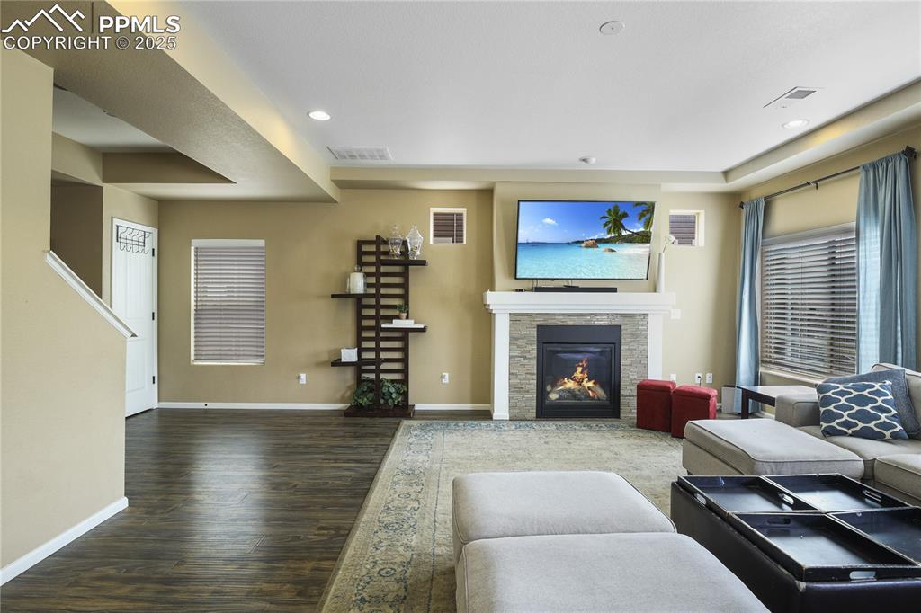 Image 10 of 38: Living room featuring a stone fireplace and dark wood-type flooring