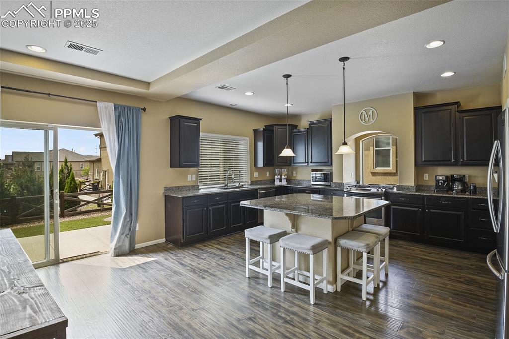 Image 12 of 38: Kitchen with dark wood-type flooring, dark stone counters, sink, hanging li