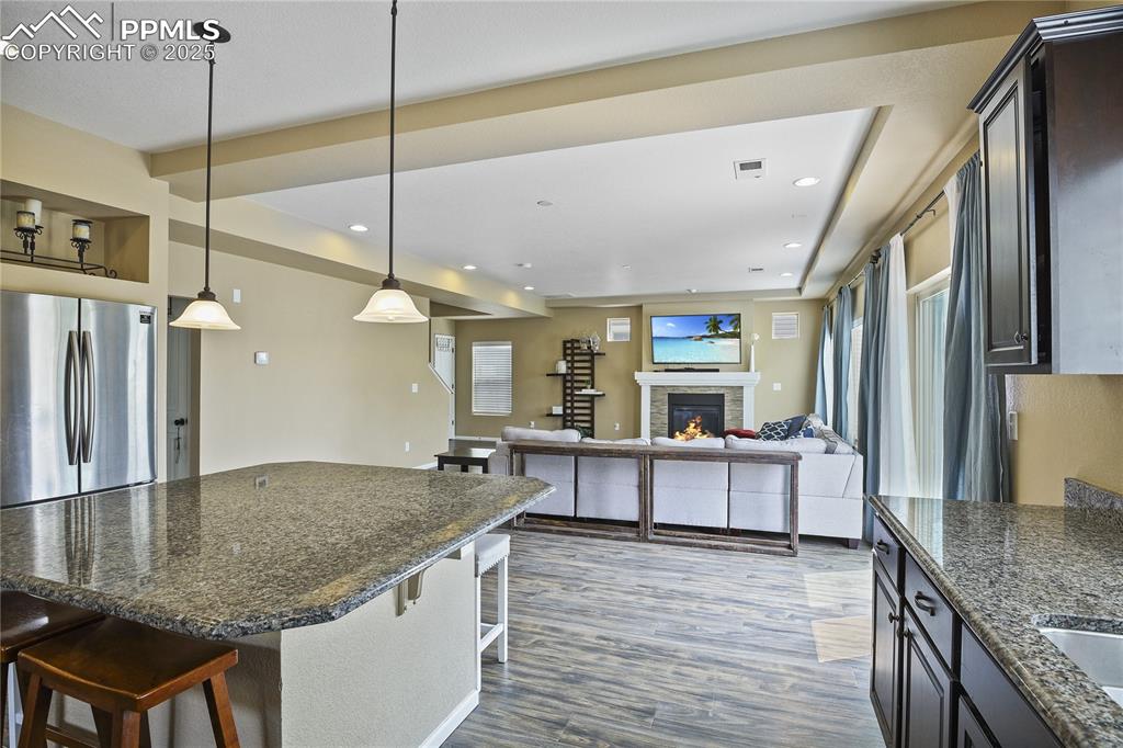 Image 16 of 38: Kitchen with pendant lighting, dark wood-type flooring, a stone fireplace,