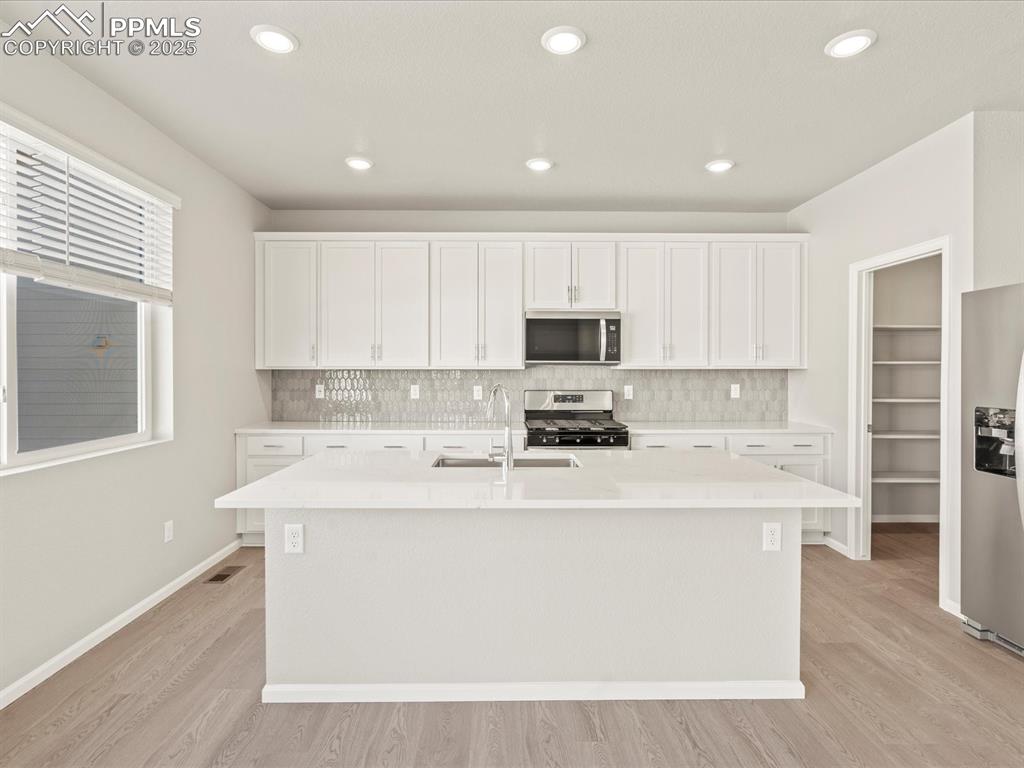 Image 2 of 26: Kitchen featuring tasteful backsplash, white cabinetry, an island with sink