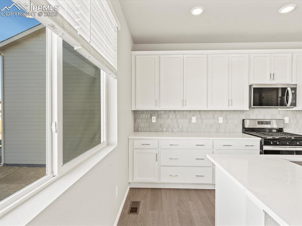 Image 4 of 26: Kitchen featuring white cabinetry, stainless steel appliances, light stone