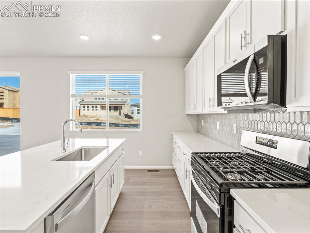 Image 6 of 26: Kitchen with appliances with stainless steel finishes, white cabinetry, lig