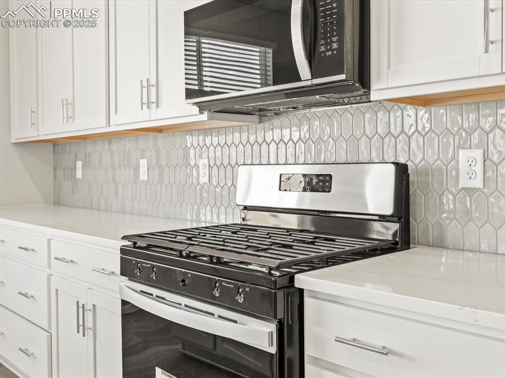 Image 7 of 26: Kitchen with stainless steel appliances, backsplash, white cabinetry, and l