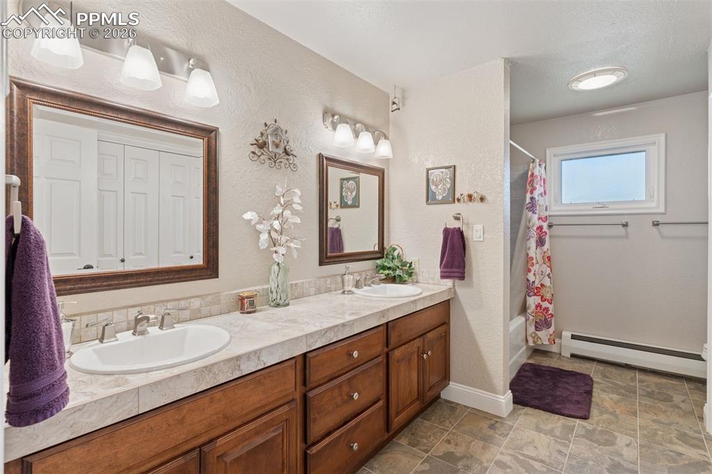 Image 19 of 50: Full bathroom with double vanity, shower / bath combo, a textured wall, and