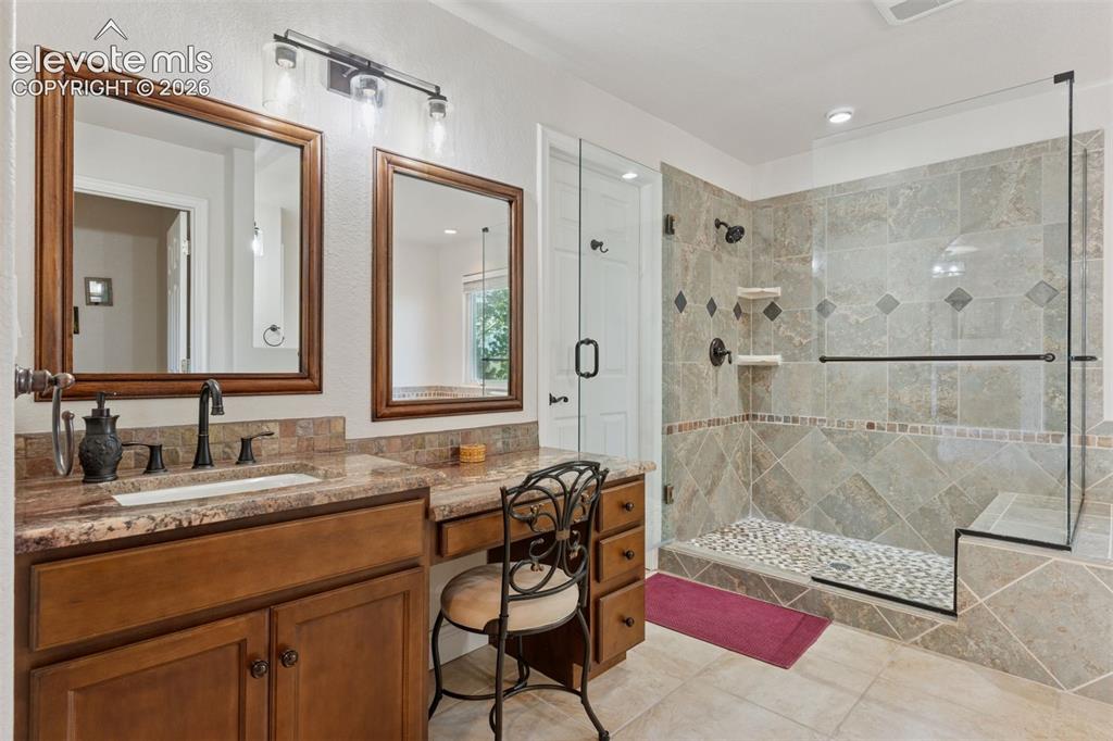 Image 39 of 50: Primary bath with heated floors, multiple vanities, a stall shower w/bench