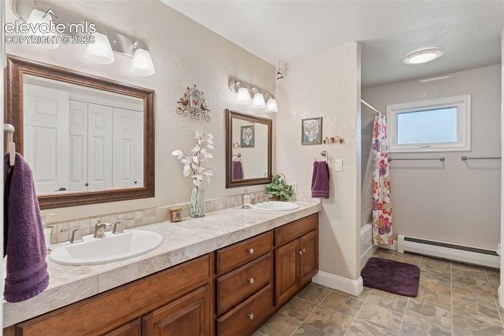 Image 42 of 50: Additional full bathroom with double vanity, shower / bath combo, a texture