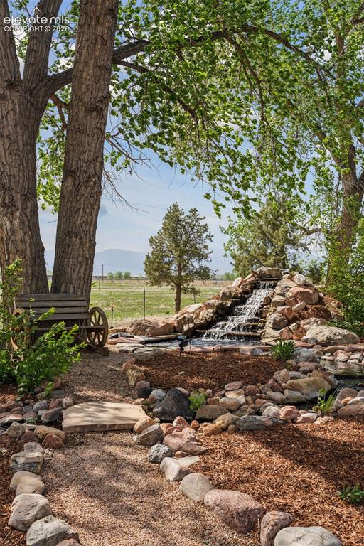 Image 7 of 50: Waterfall Feature w/babbling brook and antique wheel bench in Front of Resi