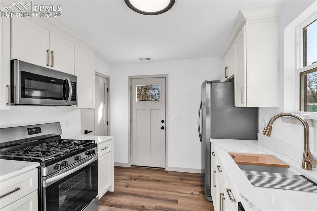 Image 10 of 39: Kitchen with stainless steel appliances, white cabinets, dark wood-style fl
