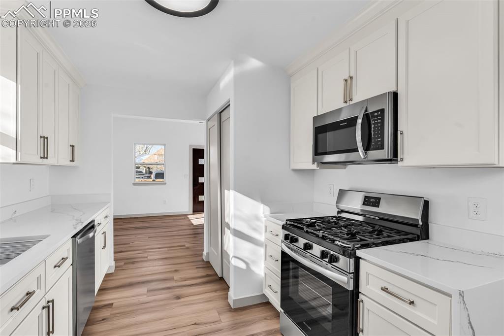 Image 11 of 39: Kitchen featuring stainless steel appliances, white cabinets, light stone c