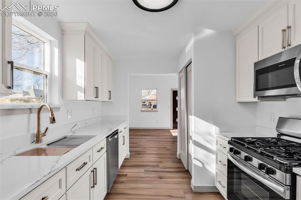 Image 12 of 39: Kitchen featuring stainless steel appliances, white cabinetry, light stone