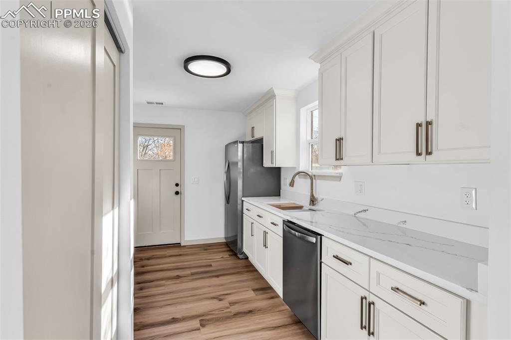 Image 9 of 39: Kitchen with white cabinetry, stainless steel appliances, light wood-style