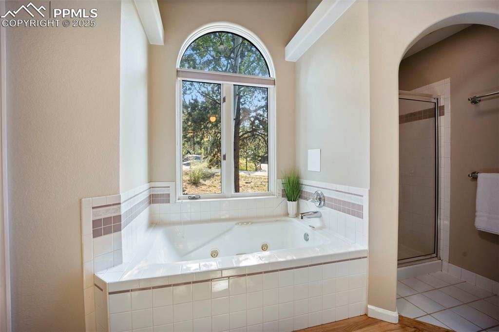 Image 17 of 33: Bathroom with a stall shower, a whirlpool tub, and wood finished floors