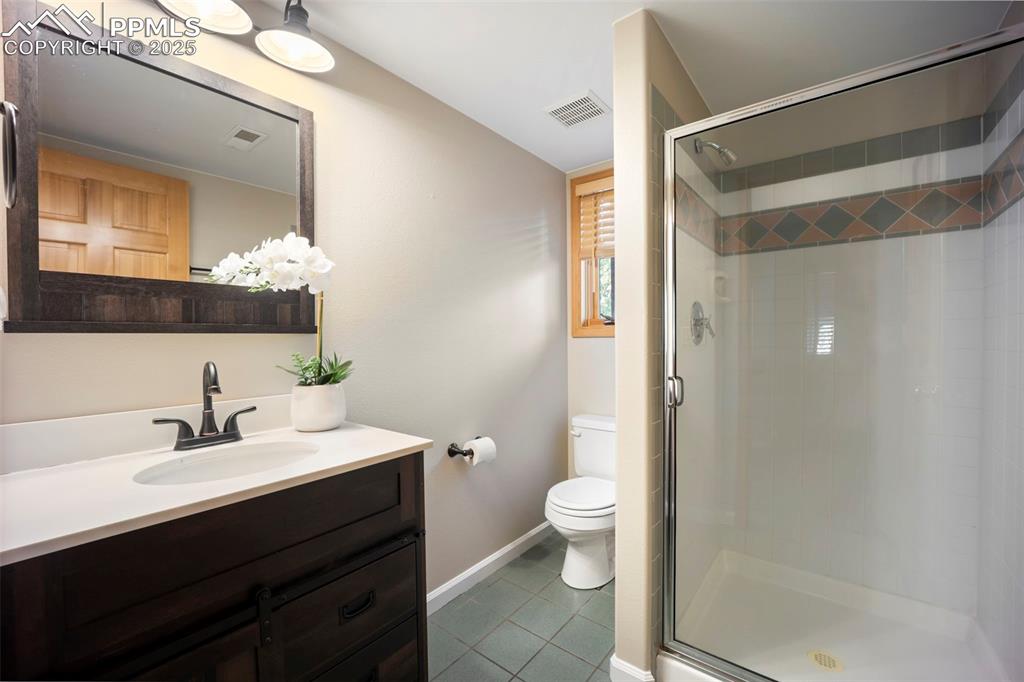 Image 20 of 33: Full bath featuring dark tile patterned floors, vanity, and a shower stall