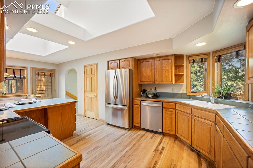 Image 7 of 33: Kitchen featuring tile counters, brown cabinetry, recessed lighting, plenty