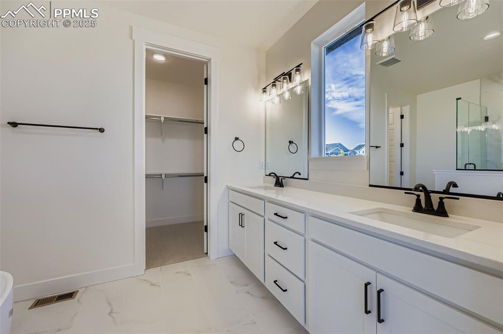 Image 14 of 28: Full bath featuring double vanity, light marble finish floors, a walk in cl