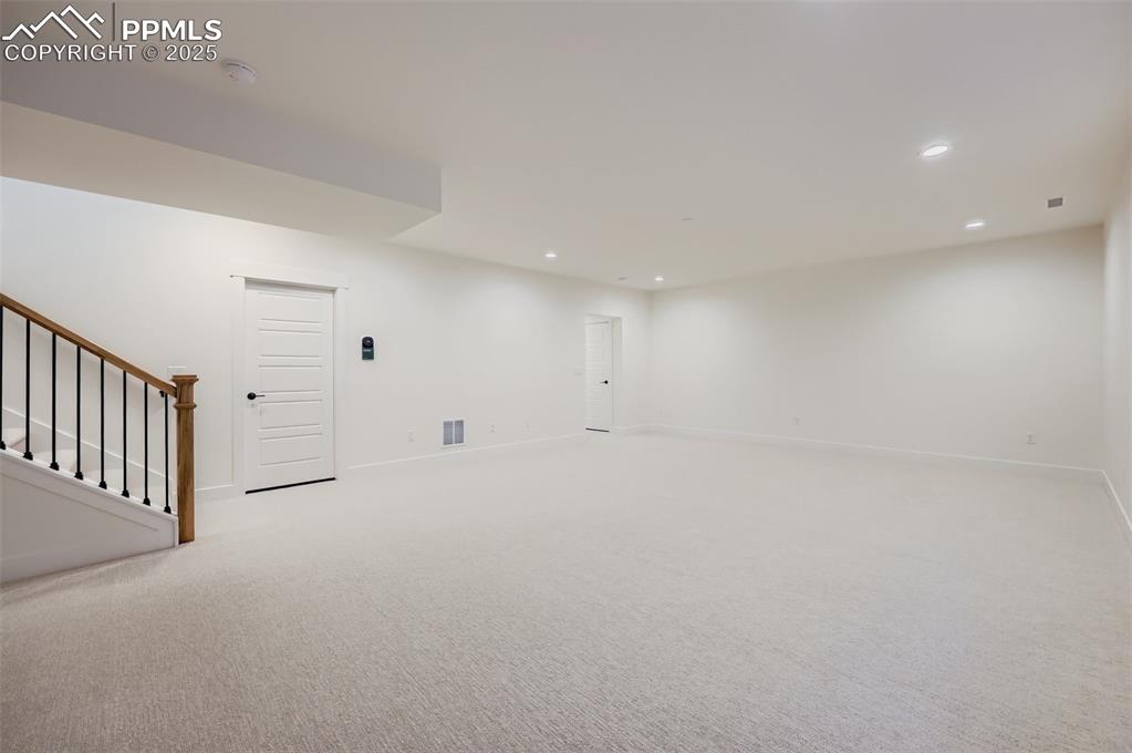 Image 19 of 28: Empty room with stairs, light colored carpet, and recessed lighting