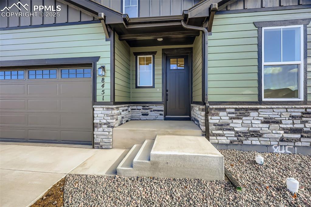 Image 3 of 28: Entrance to property with stone siding, board and batten siding, a garage,