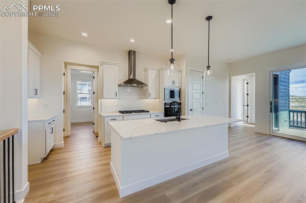 Image 7 of 28: Kitchen with white cabinets, wall chimney range hood, an island with sink,