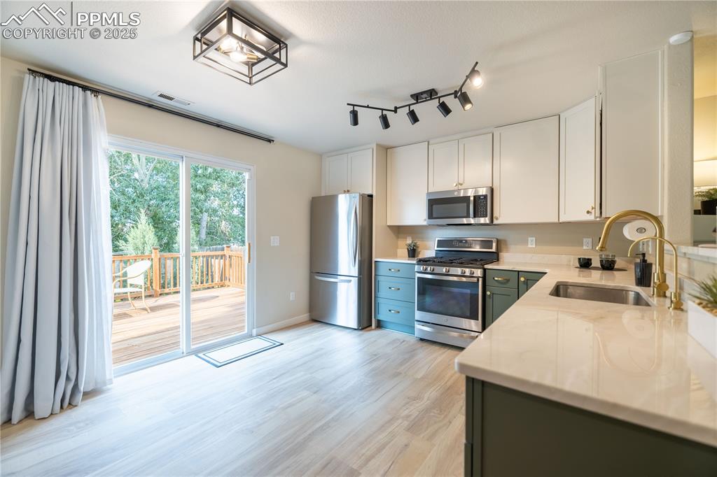 Image 10 of 42: Kitchen featuring stainless steel appliances, white cabinets, light wood-ty