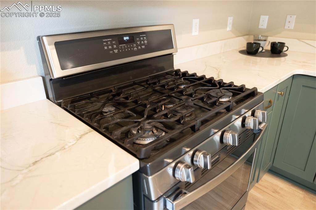 Image 14 of 42: Kitchen view of green cabinetry, gas stove, and light stone counters
