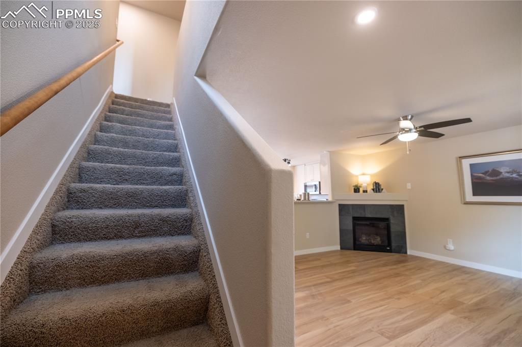 Image 18 of 42: Stairway featuring wood finished floors, a ceiling fan, and a tiled firepla
