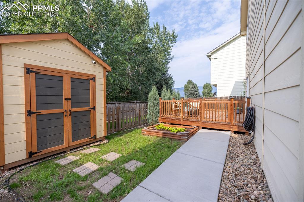 Image 35 of 42: Fenced backyard featuring a vegetable garden, a storage shed, and a deck wi